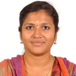 Portrait of Aarthi wearing a colorful patterned shawl and a gold necklace, posed against a plain white background.