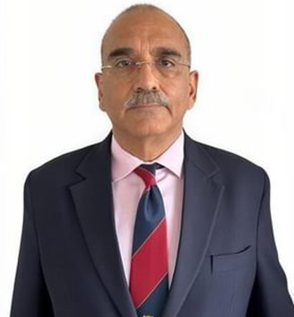 Man in a dark suit, light pink shirt, and striped tie standing against a plain white background, looking directly at the camera.