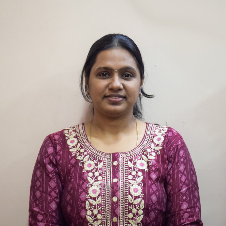 Woman in a maroon embroidered kurta standing against a plain light-colored background, facing the camera with a neutral expression.