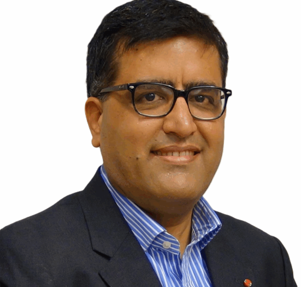 Smiling man in a dark blazer and blue striped shirt wearing glasses, posing against a plain light background.