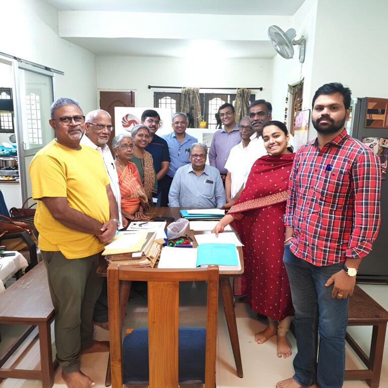 Group of professionals and family members gathered around a table in a home-office setting, smiling and facing the camera.