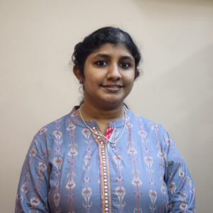 Woman in a blue patterned kurta standing against a plain light-colored background, facing the camera.